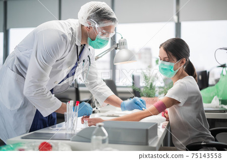 In a private clinic nurse a man puts a tourniquet on the arm of a female patient and takes blood from a vein for analysis In a private clinic nurse a man puts a tourniquet on the arm of a female patient and takes blood from a vein for analysis 75143558