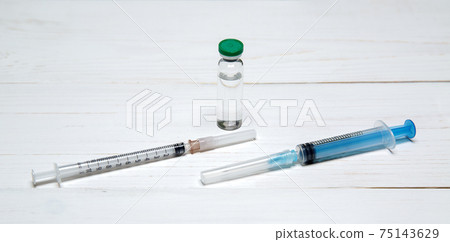 two syringes for injections and bottle with a vaccine lie on light wooden table two syringes for injections and bottle with a vaccine lie on light wooden table 75143629