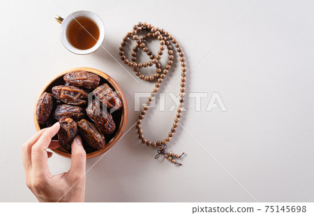 Top view image of decoration Ramadan Kareem background,  hands picking up dates fruit, tea and rosary beads. Flat lay background with copy space. 75145698