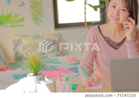 A woman who smiles and takes notes while calling A woman who smiles and takes notes while calling 75147258