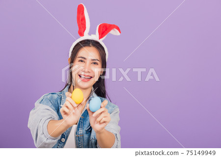 woman smiling wearing rabbit ears and denims hold colorful Easter eggs gift on hands woman smiling wearing rabbit ears and denims hold colorful Easter eggs gift on hands 75149949