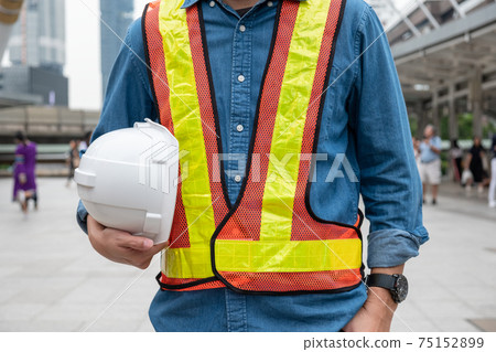 Constructor man in work vest holding safety helmet at workplace 75152899