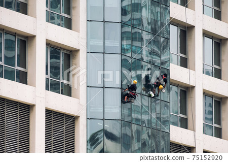 Group of worker men hanging sling with cleaning the window of modern building Group of worker men hanging sling with cleaning the window of modern building 75152920