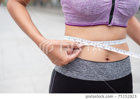 Asian oman in sportswear using tape measure around woman abdomen Asian oman in sportswear using tape measure around woman abdomen 75152923