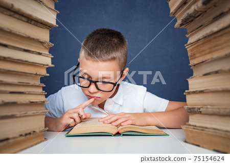 Smart boy in glasses sitting between two piles of books and read Smart boy in glasses sitting between two piles of books and read 75154624