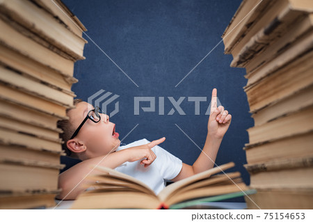 Smart boy in glasses sitting between two piles of books and look 75154653