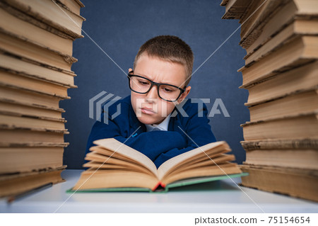Smart boy in glasses sitting between two piles of books and read Smart boy in glasses sitting between two piles of books and read 75154654
