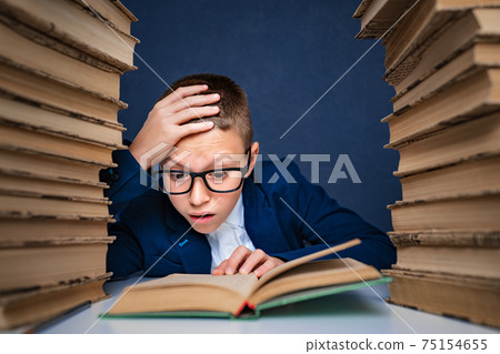 Smart boy in glasses sitting between two piles of books and read Smart boy in glasses sitting between two piles of books and read 75154655