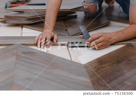 Man laying parquet flooring - closeup on male hands. worker joining parquet floor 75156300
