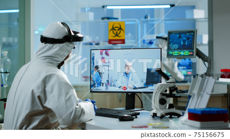 Chemist in ppe suit listening professional doctor on video call Chemist in ppe suit listening professional doctor on video call 75156675