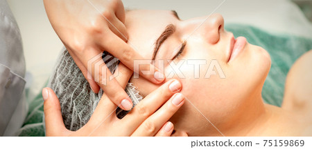 Young woman receiving facial massage 75159869
