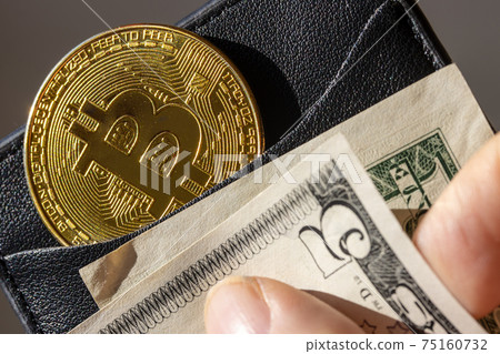 A Gold bitcoin coin tucked in a wallet with dollar bills. 75160732