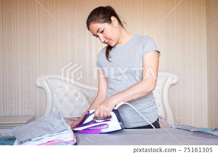 Young smiling woman ironing things with iron Young smiling woman ironing things with iron 75161305