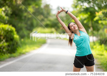 Healthy woman warming up before jogging run and relax stretching her arms and looking away in the road outdoor.  75164839