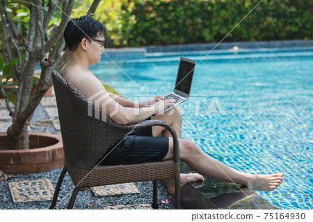 asian businessman seat a chair working with laptop in swimming poolside. work new normal. asian businessman seat a chair working with laptop in swimming poolside. work new normal. 75164930