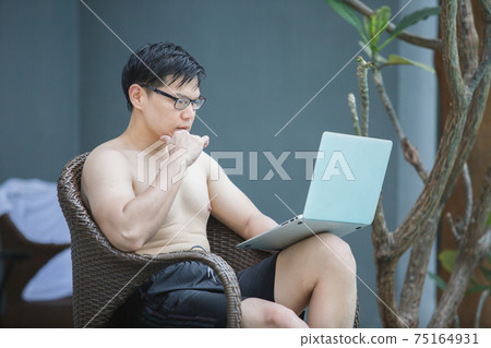 asian businessman seat a chair not wear a shirt working with laptop in swimming poolside. asian businessman seat a chair not wear a shirt working with laptop in swimming poolside. 75164931
