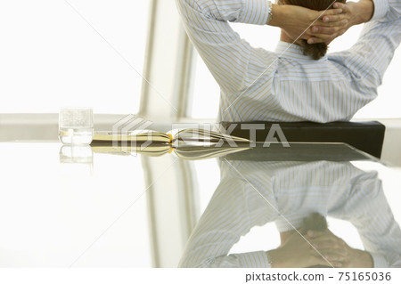 Businessman with hands behind head in office 75165036