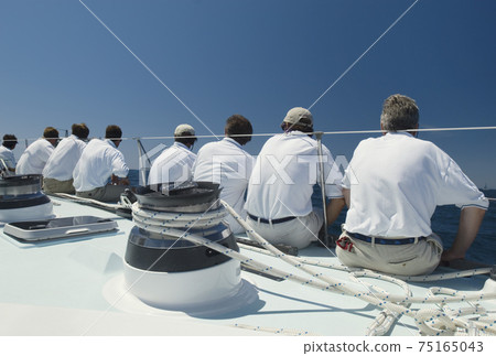 Sailing crew sitting on side of yacht on ocean back view Sailing crew sitting on side of yacht on ocean back view 75165043