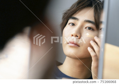 Image of young men's men's makeup applying cream foundation to cheeks 75166068