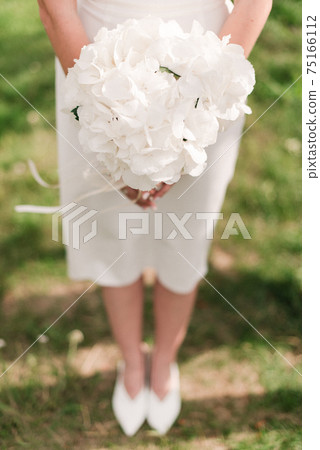 the bride is holding a wedding bouquet in a white dress the bride is holding a wedding bouquet in a white dress 75166112