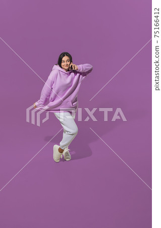 High angle view of young woman on purple studio background. Girl in motion or movement. Human emotions and facial expressions concept 75166412