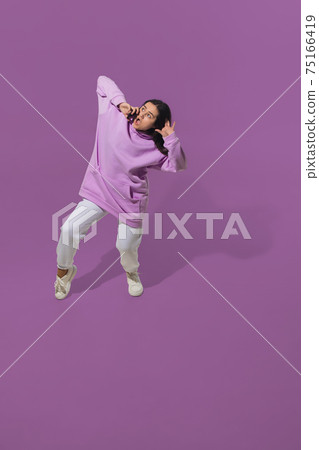 High angle view of young woman on purple studio background. Girl in motion or movement. Human emotions and facial expressions concept High angle view of young woman on purple studio background. Girl in motion or movement. Human emotions and facial expressions concept 75166419