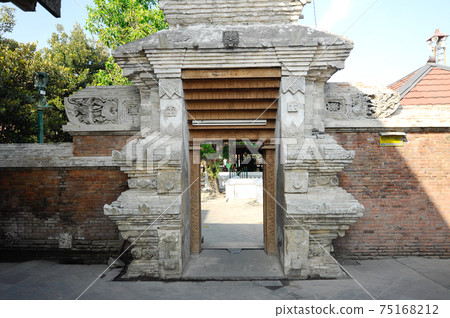 JOGJAKARTA, INDONESIA -JUNE 12, 2014: Entrance arch at old Masjid Besar Mataram Kotagede, Jogjakarta Indonesia. The arch was made from brick and hand made carving stone in traditional Balinese Style JOGJAKARTA, INDONESIA -JUNE 12, 2014: Entrance arch at old Masjid Besar Mataram Kotagede, Jogjakarta Indonesia. The arch was made from brick and hand made carving stone in traditional Balinese Style 75168212