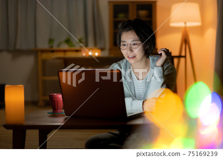 看一台計算機的一個微笑的少婦在客廳在晚上 75169239
