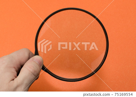Hand with magnifying glass on orange background 75169554