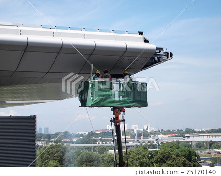 JOHOR, MALAYSIA -MAY 16, 2017: Construction workers standing in the mobile crane bucket while working at high level in the construction site. The bucket movement control by the workers himself. JOHOR, MALAYSIA -MAY 16, 2017: Construction workers standing in the mobile crane bucket while working at high level in the construction site. The bucket movement control by the workers himself. 75170140