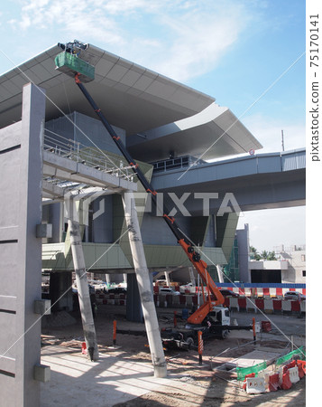 JOHOR, MALAYSIA -MAY 16, 2017: Construction workers standing in the mobile crane bucket while working at high level in the construction site. The bucket movement control by the workers himself. JOHOR, MALAYSIA -MAY 16, 2017: Construction workers standing in the mobile crane bucket while working at high level in the construction site. The bucket movement control by the workers himself. 75170141