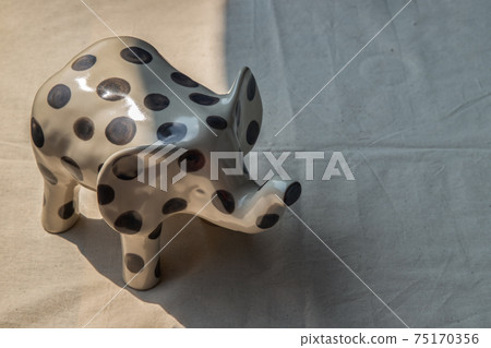 Elephants shaped ceramic on white textured table cloth. 75170356