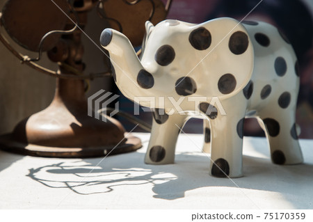 Elephants shaped ceramic and Vintage metal fan on white textured table cloth. 75170359