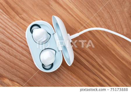 Wireless headphones on a wooden background. Headset close up in the charging case close-up. 75173888