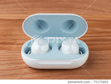 Wireless headphones on a wooden background. Headset close up in the charging case close-up. 75173891