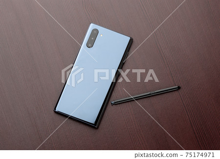 Smartphone with three cameras and a stylus on a wooden table close-up. 75174971