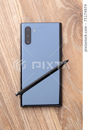 Smartphone with three cameras and a stylus on a wooden table close-up. 75174974