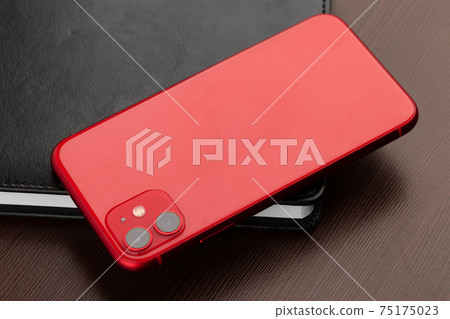 Smartphone with red color on a wooden table close-up. 75175023