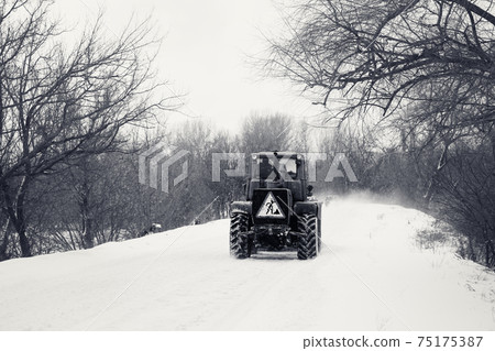 Black and white old tractor clears the snow-covered road from snow blockages 75175387