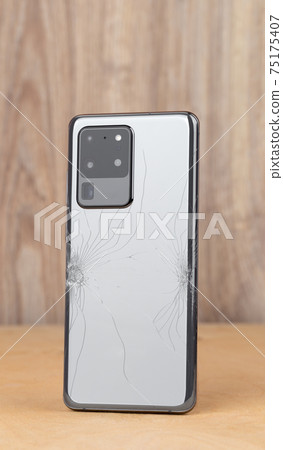 Smartphone with a broken back cover on a wooden background. Smartphone with a broken back cover on a wooden background. 75175407