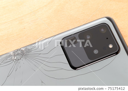 Smartphone with a broken back cover on a wooden background. 75175412