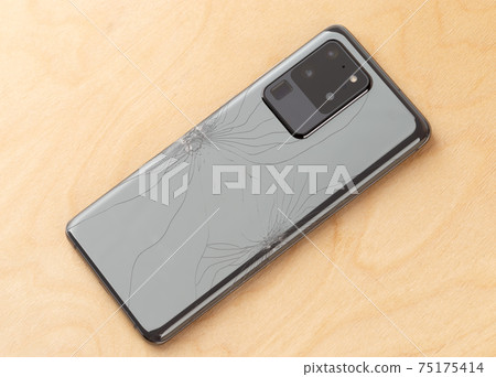 Smartphone with a broken back cover on a wooden background. 75175414