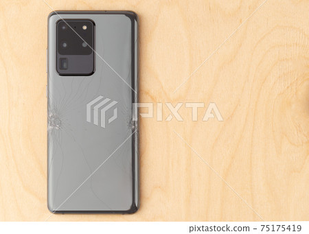 Smartphone with a broken back cover on a wooden background. 75175419