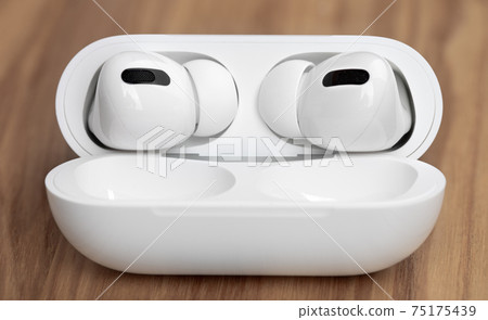 Wireless headphones on a wooden table. Wireless headset and charging case close-up. 75175439