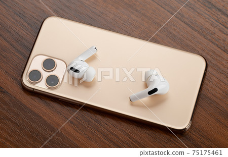Smartphone on a wooden surface. A popular smartphone and wireless headset close-up. Smartphone on a wooden surface. A popular smartphone and wireless headset close-up. 75175461