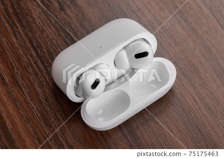Wireless headphones on a wooden table. Wireless headset and charging case close-up. Wireless headphones on a wooden table. Wireless headset and charging case close-up. 75175463