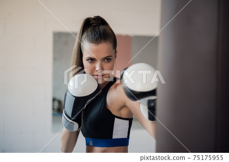 Female athlete boxing the punching bag in urban industrial gym Female athlete boxing the punching bag in urban industrial gym 75175955
