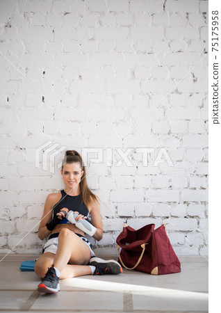 Female fighter exhausted after exercise feeling dehydration, drinks isotonic drink from bottle. Young woman rest after intense training in a boxing studio. Female fighter exhausted after exercise feeling dehydration, drinks isotonic drink from bottle. Young woman rest after intense training in a boxing studio. 75175958