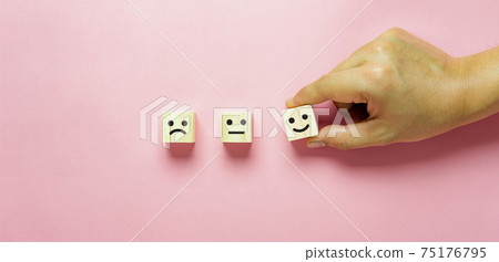 Top view of  Hand holding of Happy icon on cube blocks about rating feedback of survey from customer. Business annual survey concept. Many sad or happily on wooden on pink paper. Banner border. 75176795