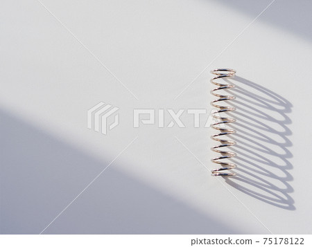 Metal mainspring on white background. Flexible chrome tube. Corrugated object on geometrical banner with copy space on hard sunlight and shadow. Metal mainspring on white background. Flexible chrome tube. Corrugated object on geometrical banner with copy space on hard sunlight and shadow. 75178122
